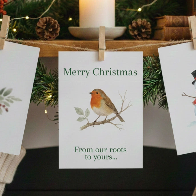 A 'Merry Christmas- From our roots to yours...' card hanging by a peg and string from a mantelpiece.
