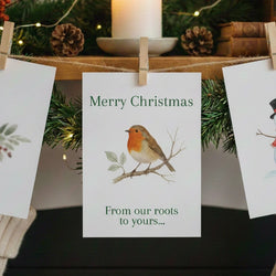 A 'Merry Christmas- From our roots to yours...' card hanging by a peg and string from a mantelpiece.