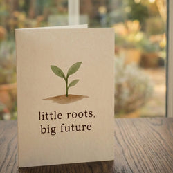 A 'little roots, big future' card from Tree2mydoor placed on a table in front of a window with a garden view.
